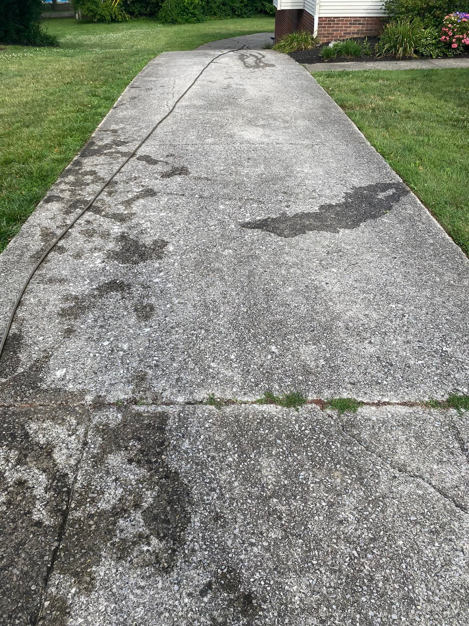 A concrete walkway leading to a house with grass on the side.