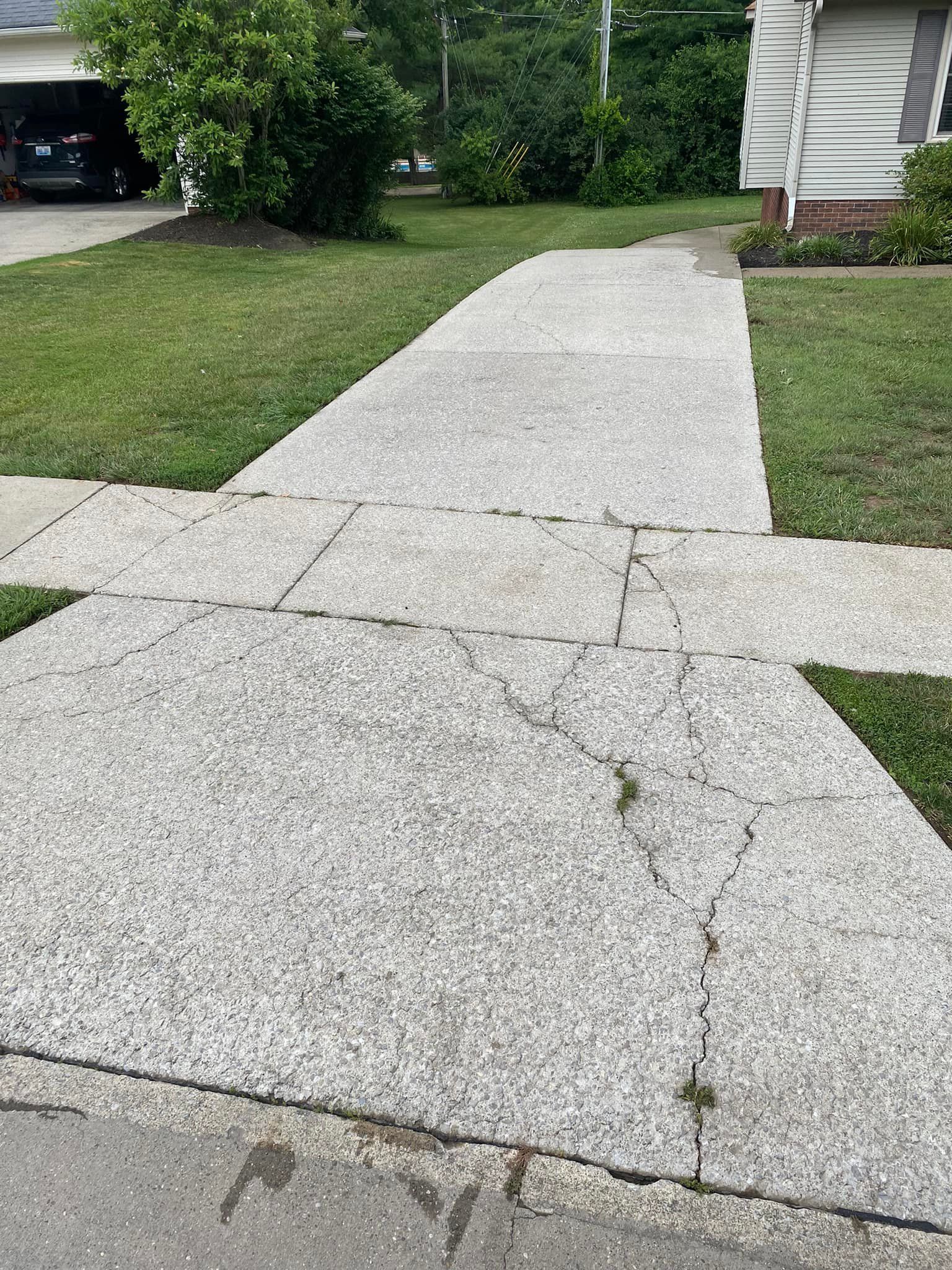 A concrete walkway leading to a house with a car parked in the driveway.