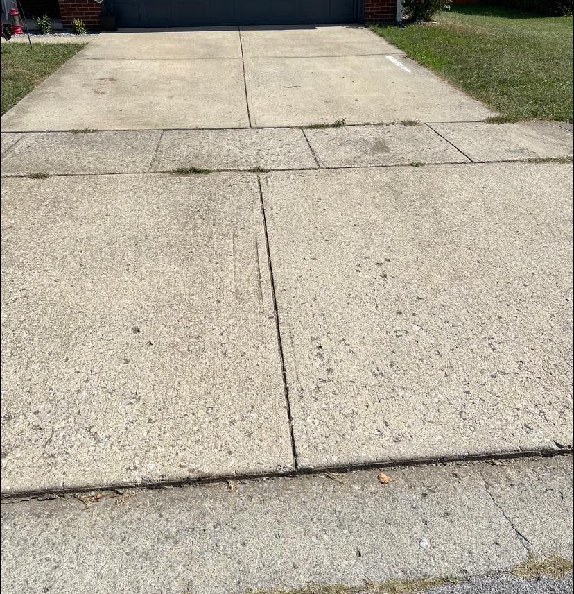 A concrete driveway leading to a garage with grass on the side of it.