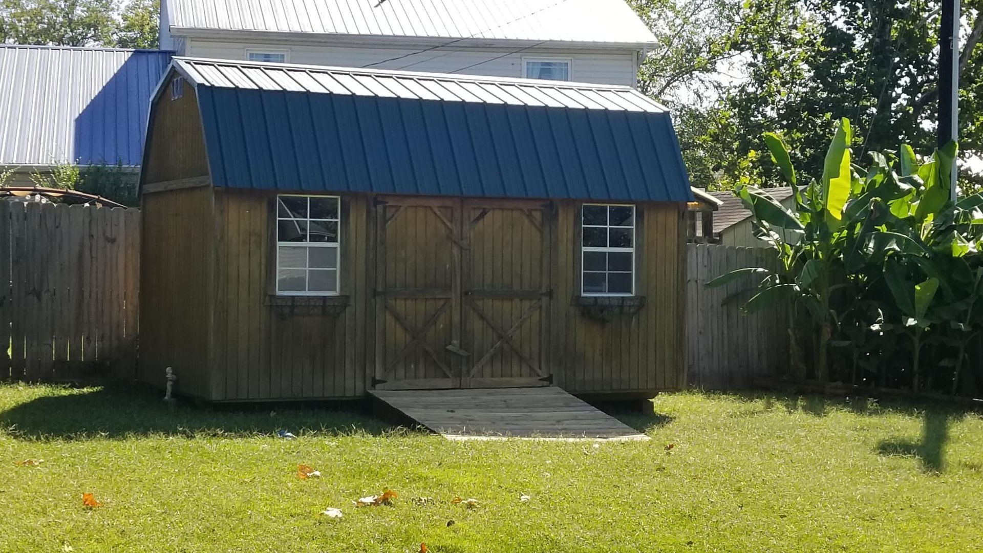 A small wooden shed with a blue roof is sitting in the grass in front of a house.