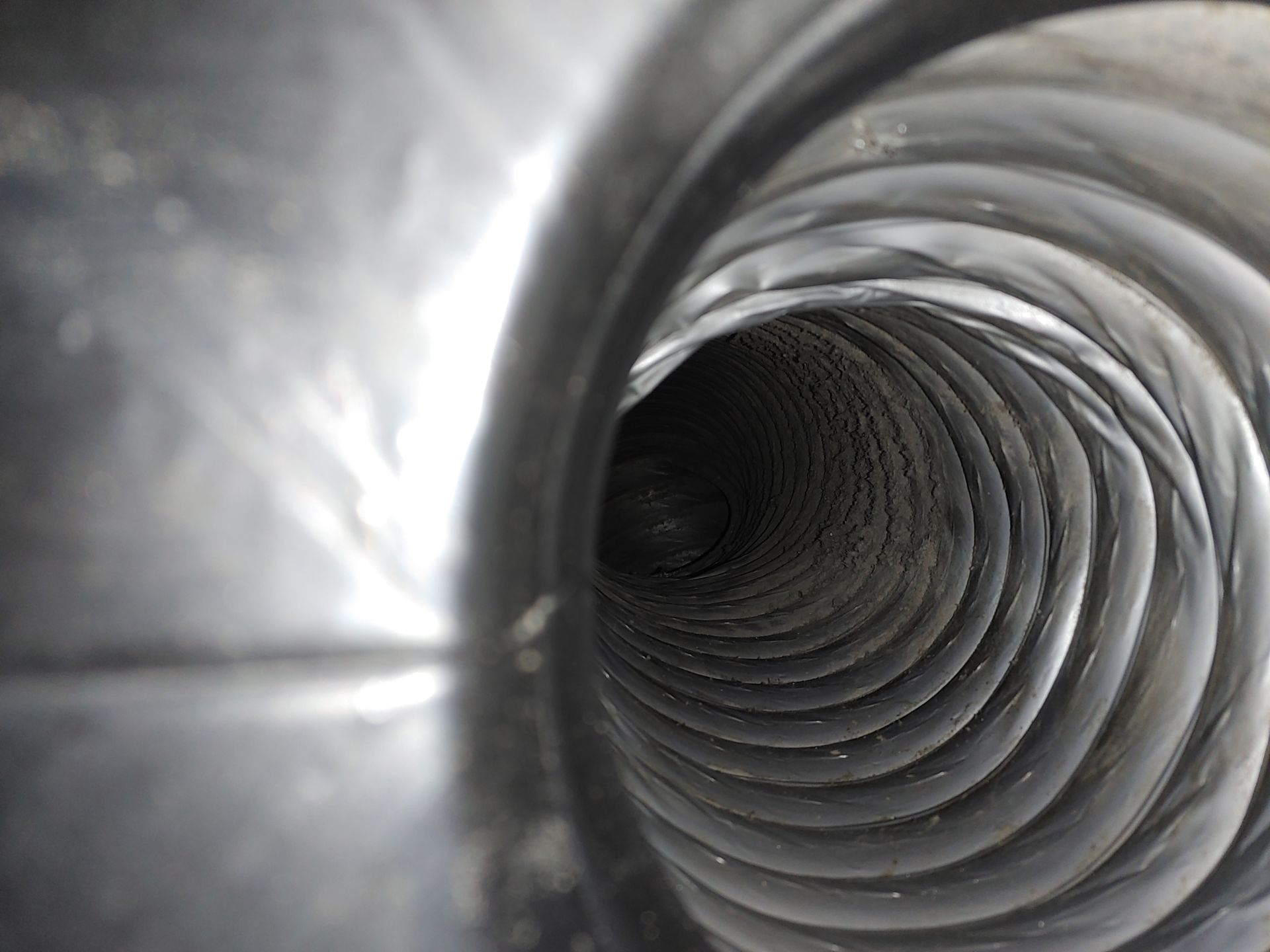 Vue intérieure d'un conduit de ventilation flexible et nervuré, intérieur sombre, forme en spirale.