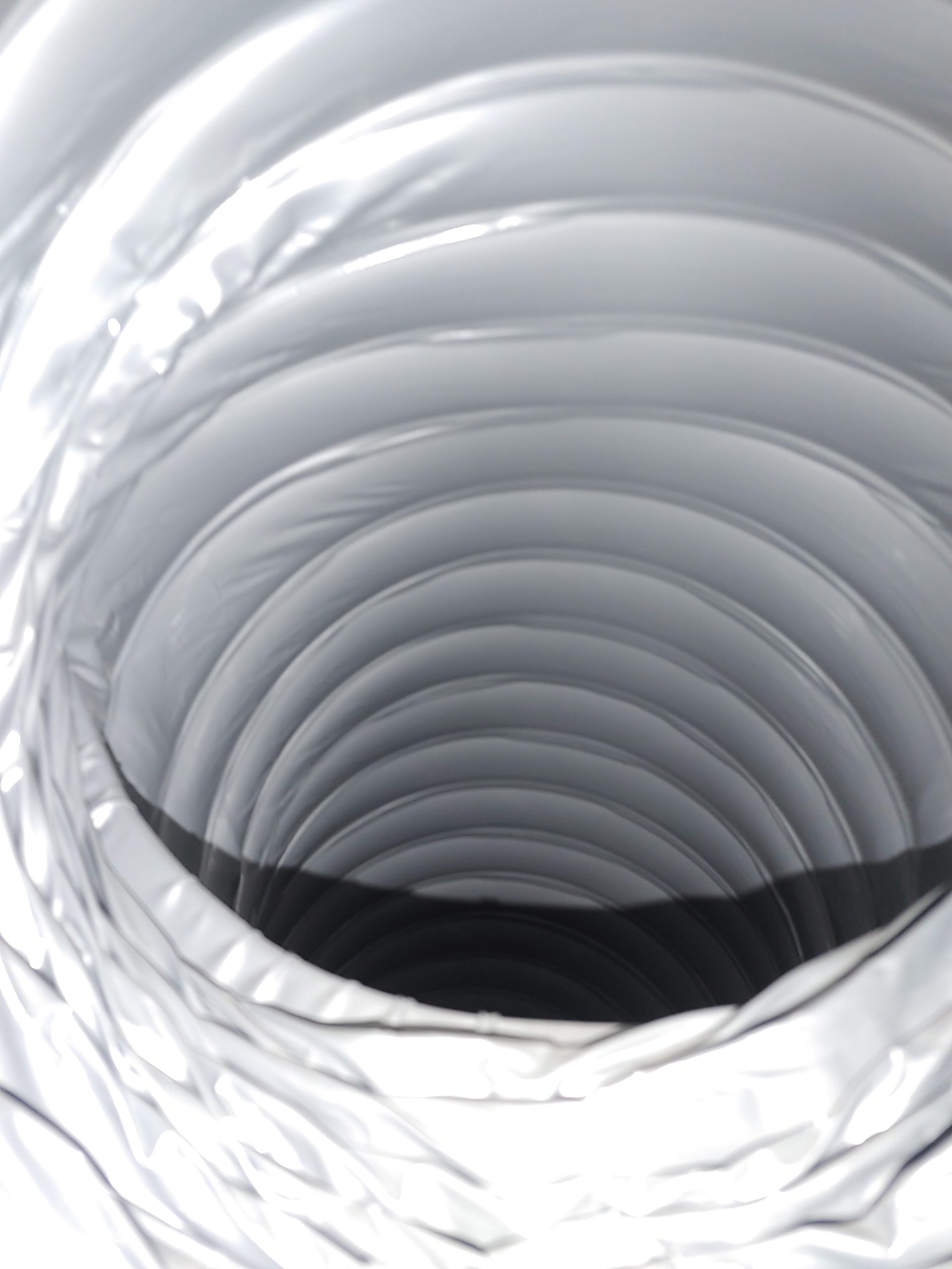 Vue intérieure d'un conduit flexible argenté aux parois ondulées, menant à une ouverture sombre.