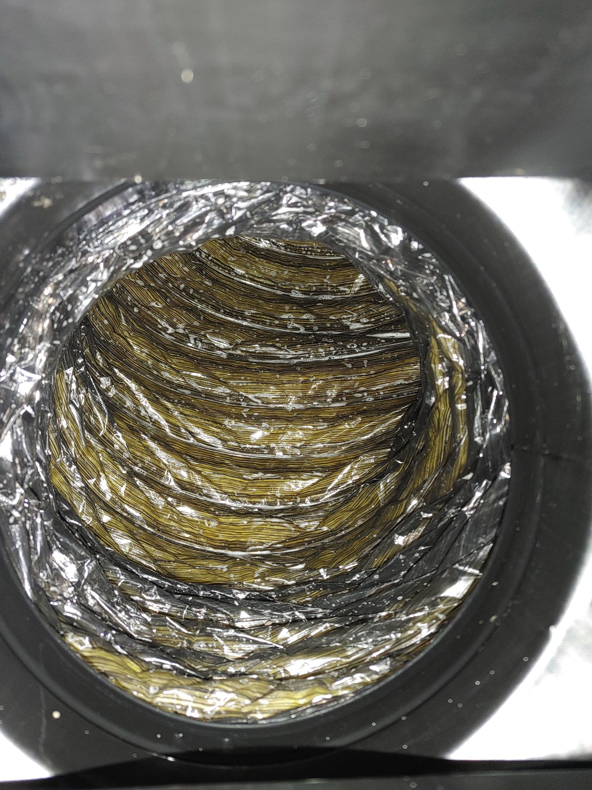 Vue intérieure d'un conduit flexible sale. L'intérieur est recouvert de crasse jaune et noire.