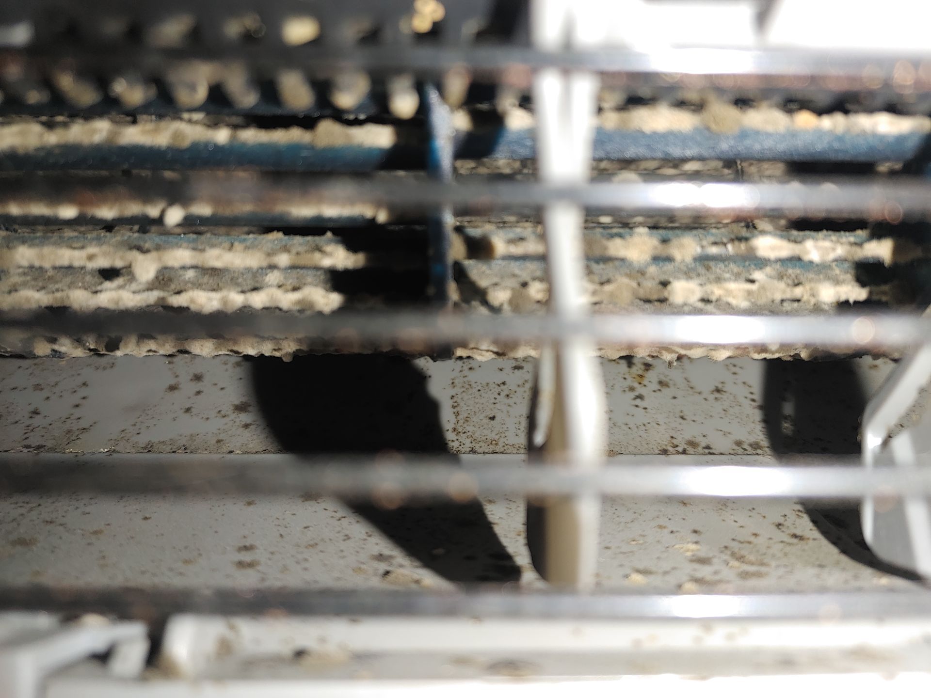 Gros plan d'une grille d'aération de climatiseur sale, avec une accumulation visible de poussière et de débris sur les ailettes.