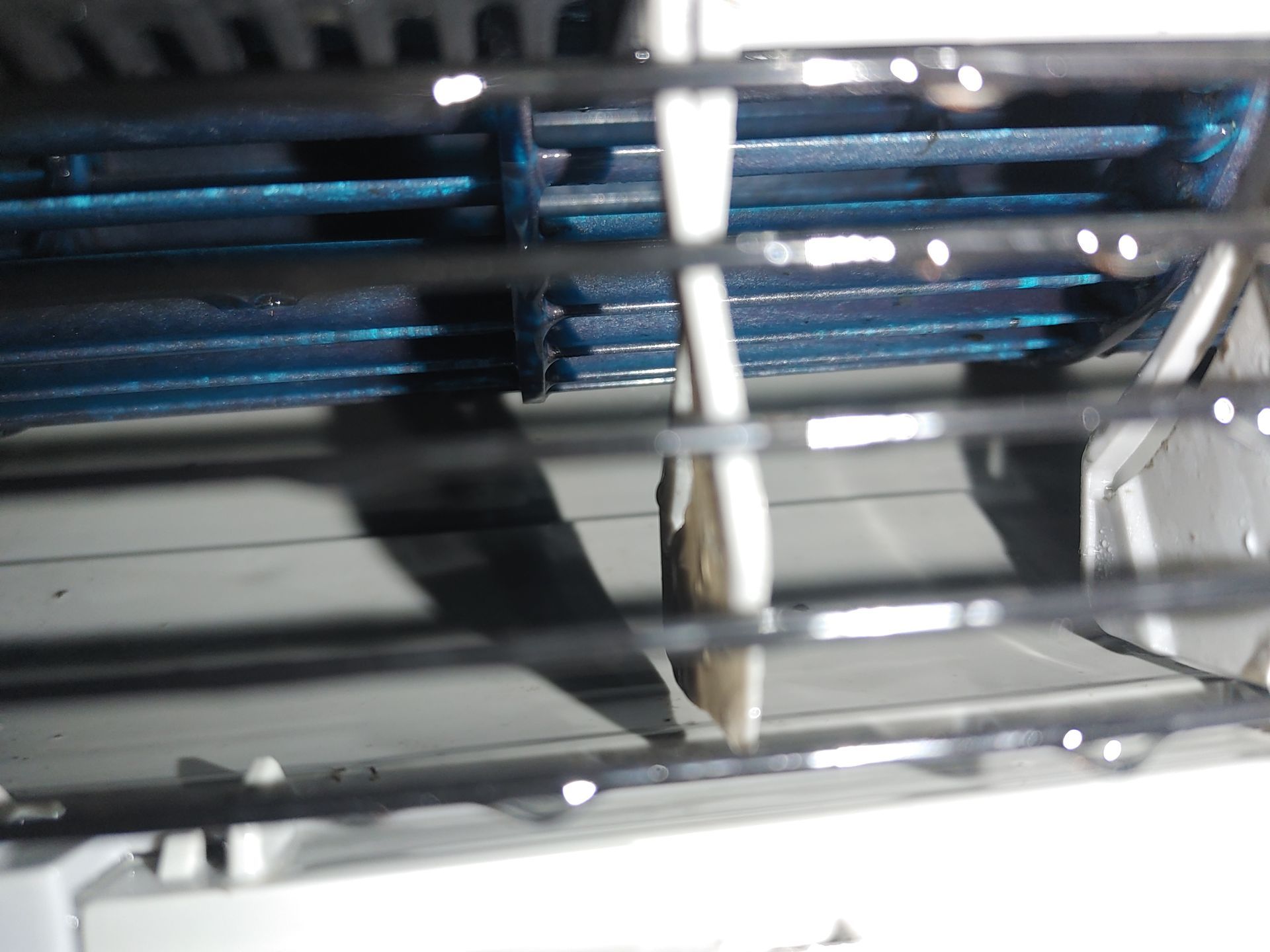 Gros plan des ailettes de refroidissement du climatiseur, de couleur bleue, visibles à travers les évents en plastique blanc.