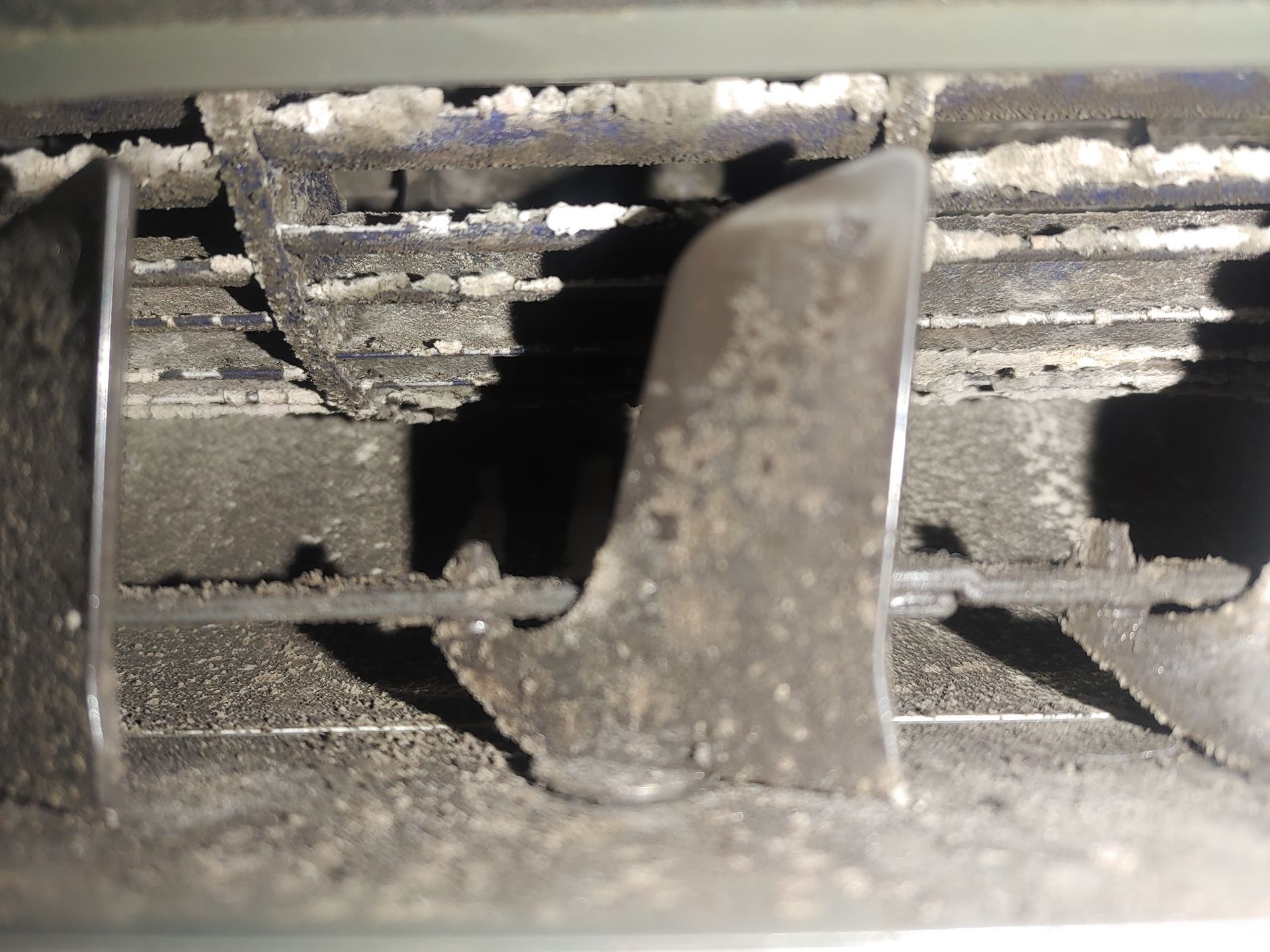 Grille d'aération sale avec accumulation de poussière visible et une ailette centrale.
