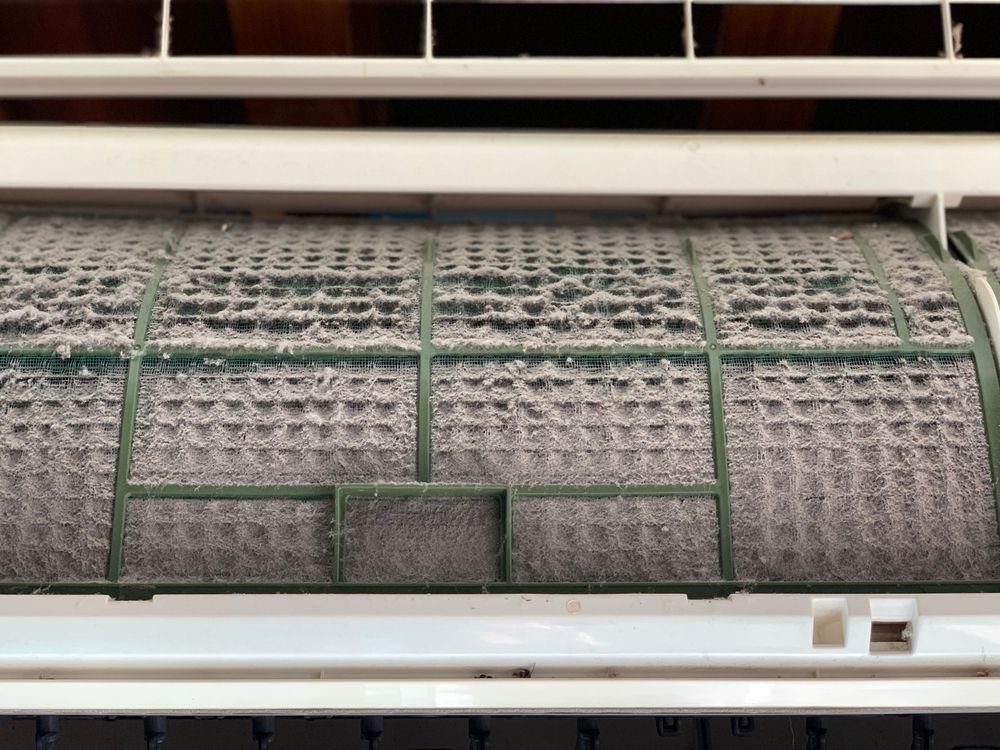 Gros plan d'un filtre de climatiseur fortement obstrué par la poussière. Cadre vert, poussière grise.