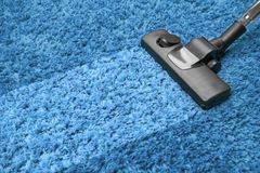 A vacuum cleaner is cleaning a blue carpet.