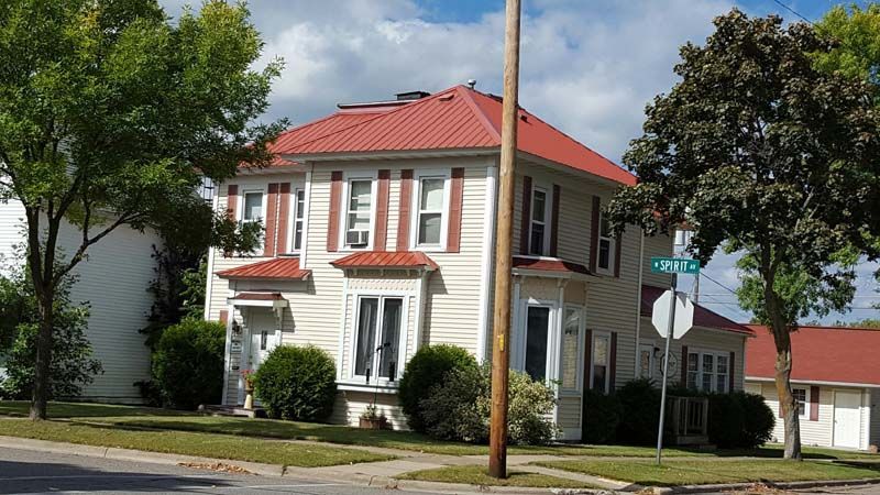 A white house with a red roof is on the corner of a street.