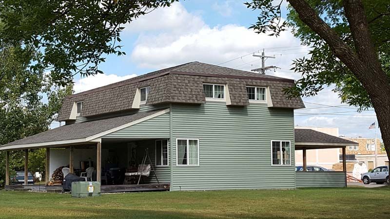 A green house with a porch and a tree in front of it