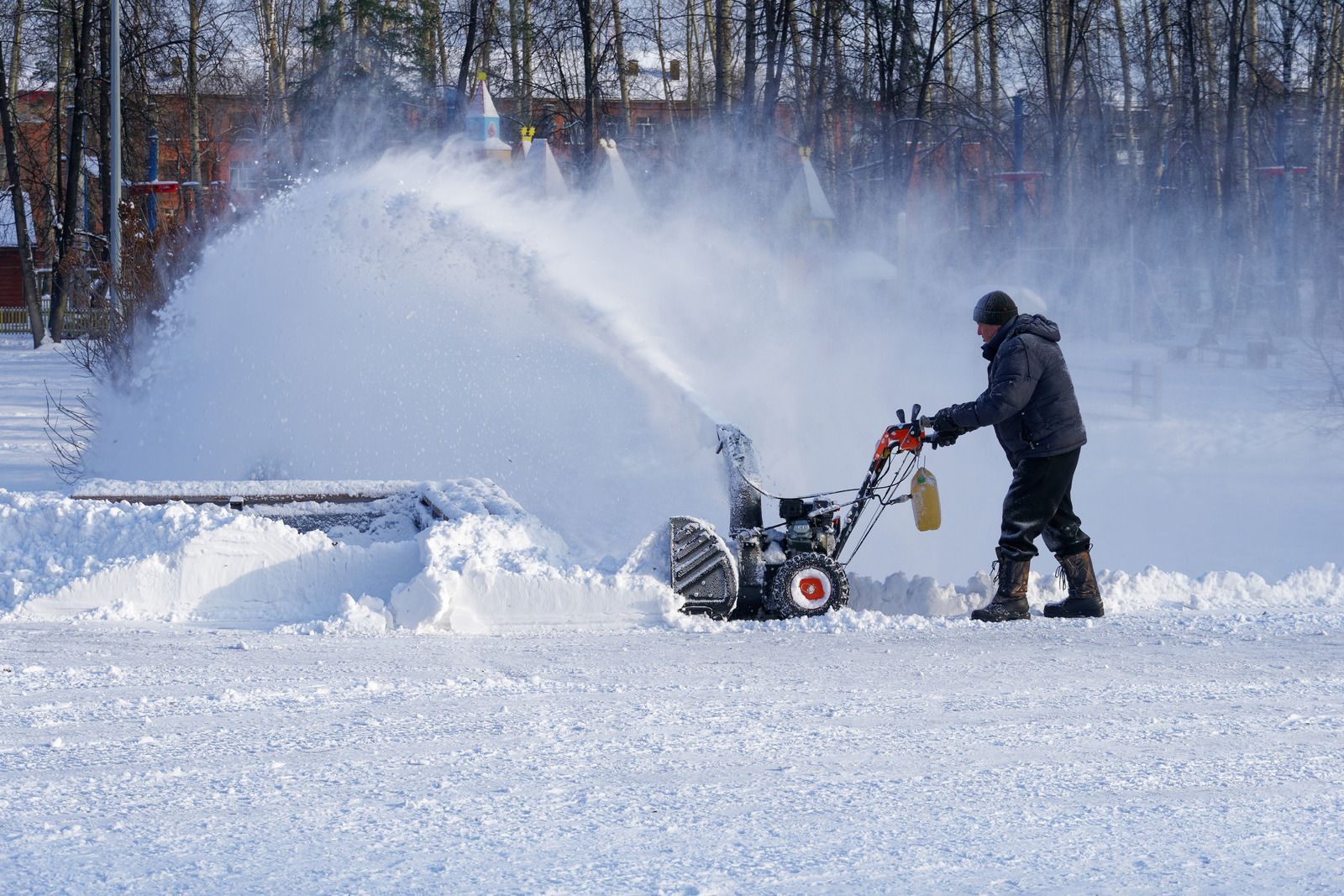 A man is blowing snow from a snow blower on a snowy field.