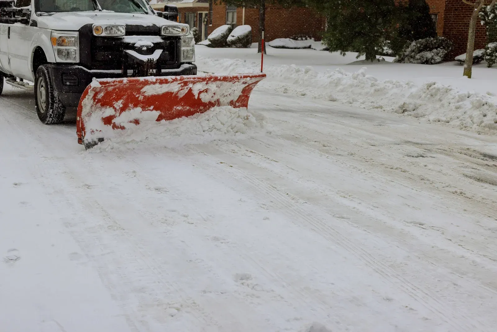 A white truck is plowing snow on a snowy street.