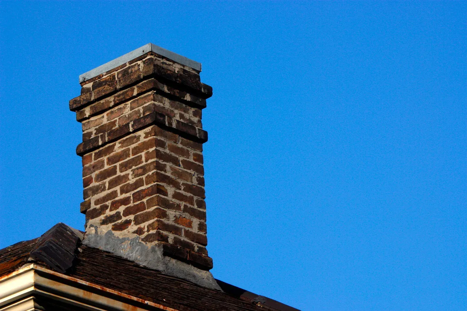 A brick chimney on top of a roof with a blue sky in the background