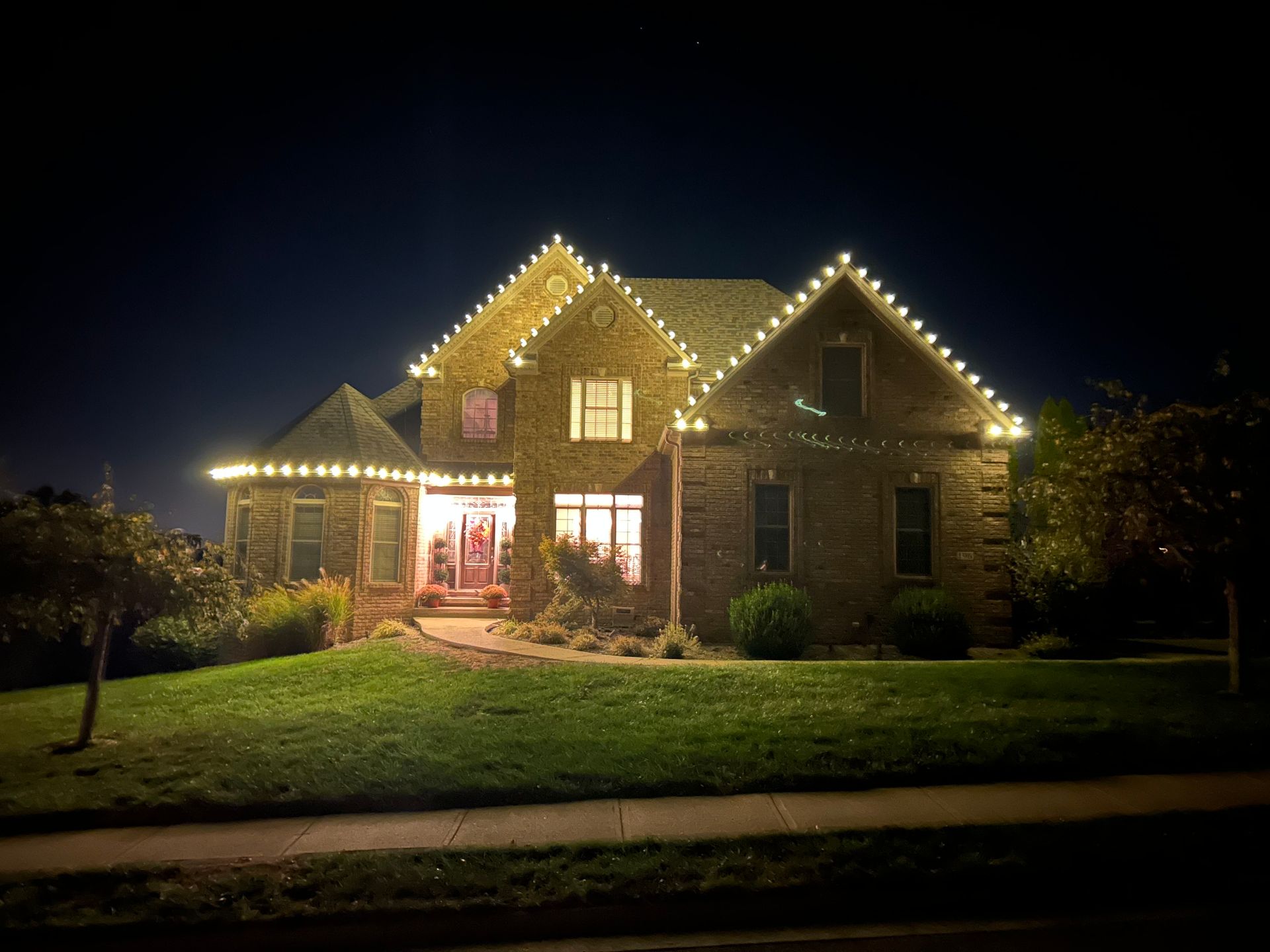 House decorated with Christmas lights, including strings, figures, and trees; nighttime.
