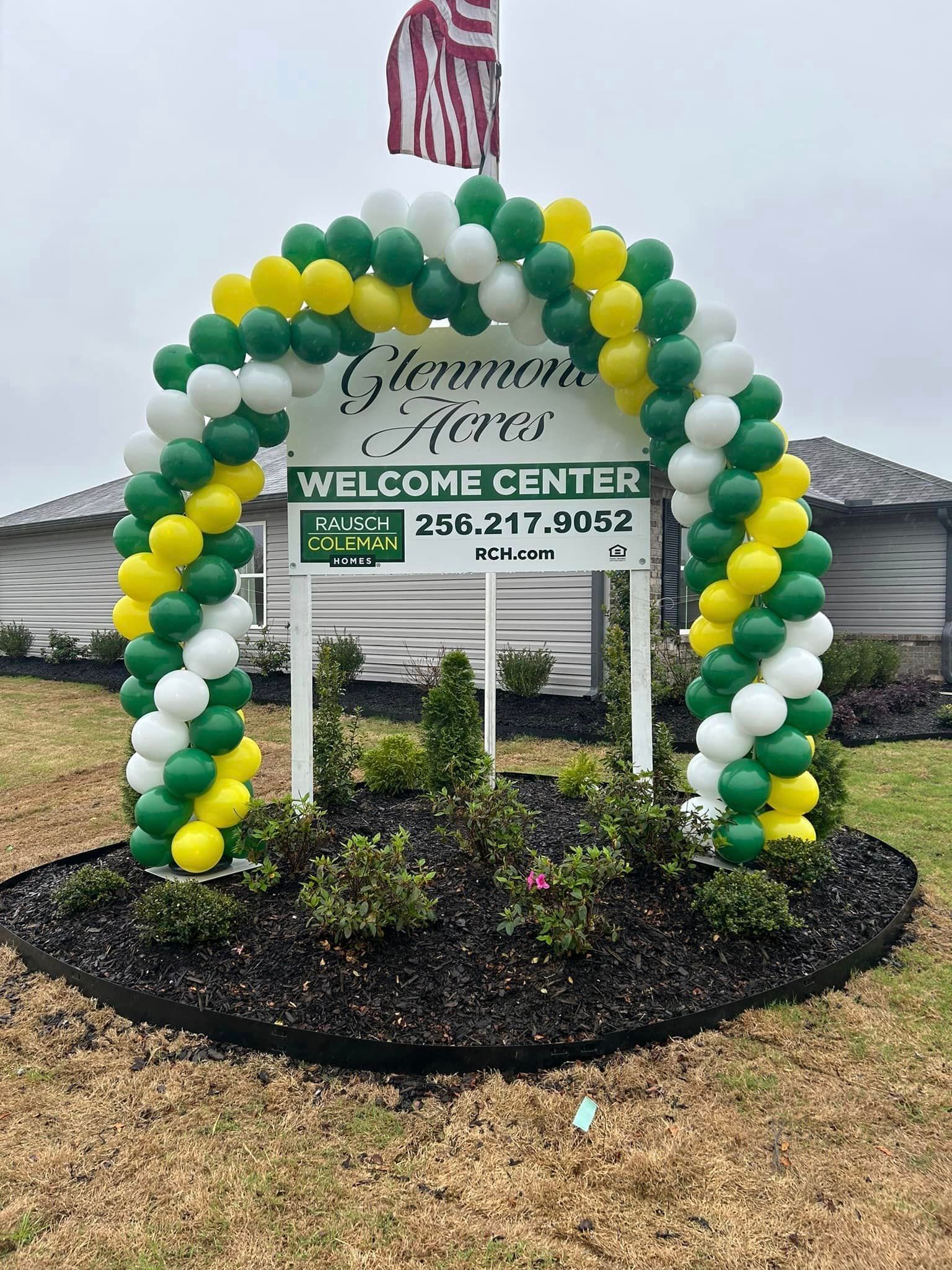 A welcome center sign is decorated with green , yellow , and white balloons.