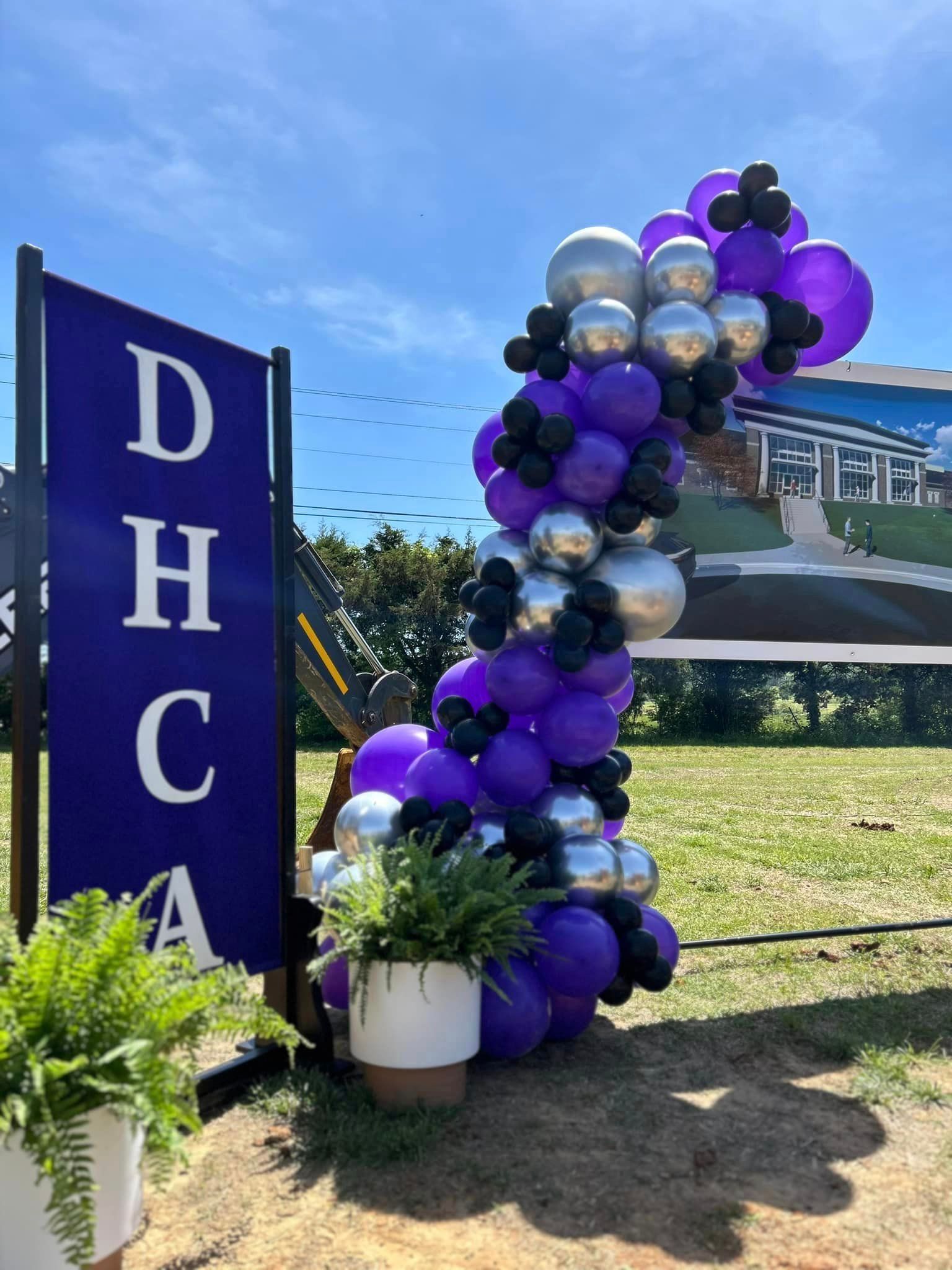 A bunch of purple and black balloons are sitting next to a sign.