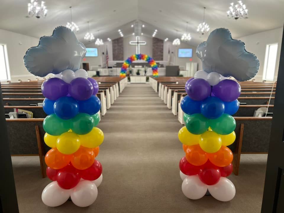 A church is decorated with rainbow colored balloons and clouds.