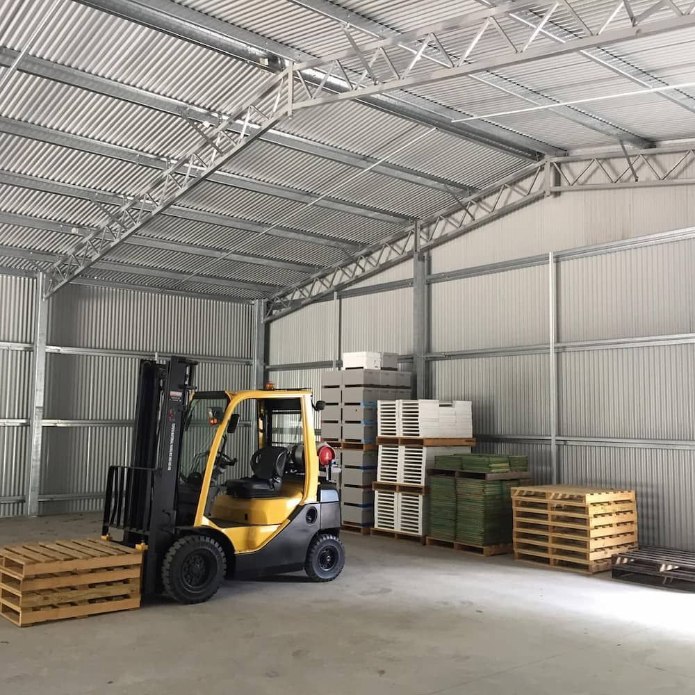 Inside a Metal Warehouse, a Yellow Forklift Sits With Wooden Pallets — Northern Rivers Sheds in South Lismore, NSW