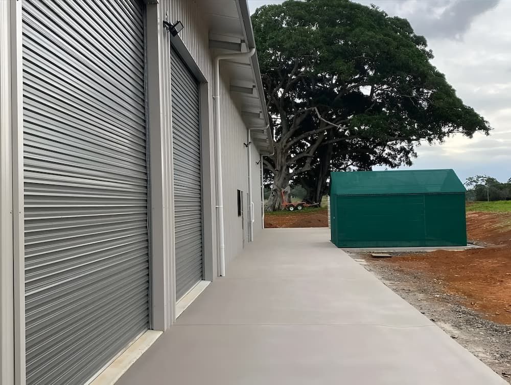 Building With Roller Doors, Concrete Path, Green Container — Northern Rivers Sheds in South Lismore, NSW