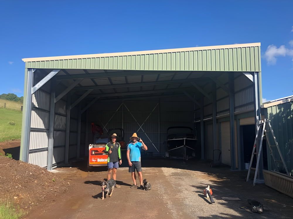 Two Men Stand in Front of a Partly Built Metal Shed With Dogs — Northern Rivers Sheds in South Lismore, NSW