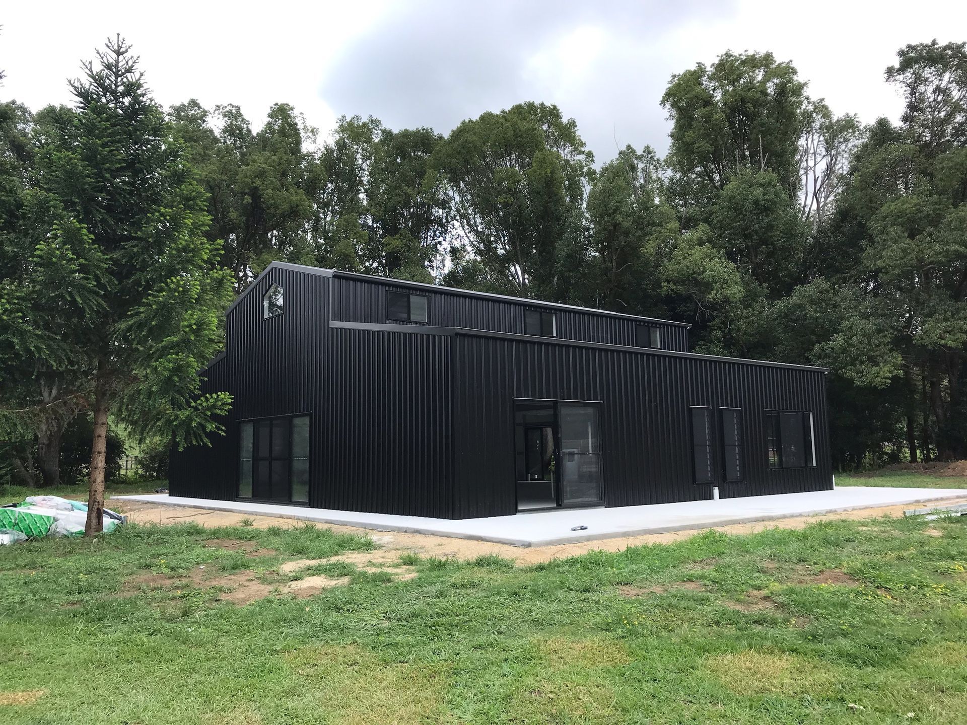 Black corrugated metal building in a Northern Rivers Sheds in South Lismore, NSW area, surrounded by trees.-
