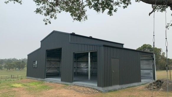 Dark gray metal barn with open bays, concrete foundation, and a tree branch overhead— Northern Rivers Sheds in South Lismore, NSW