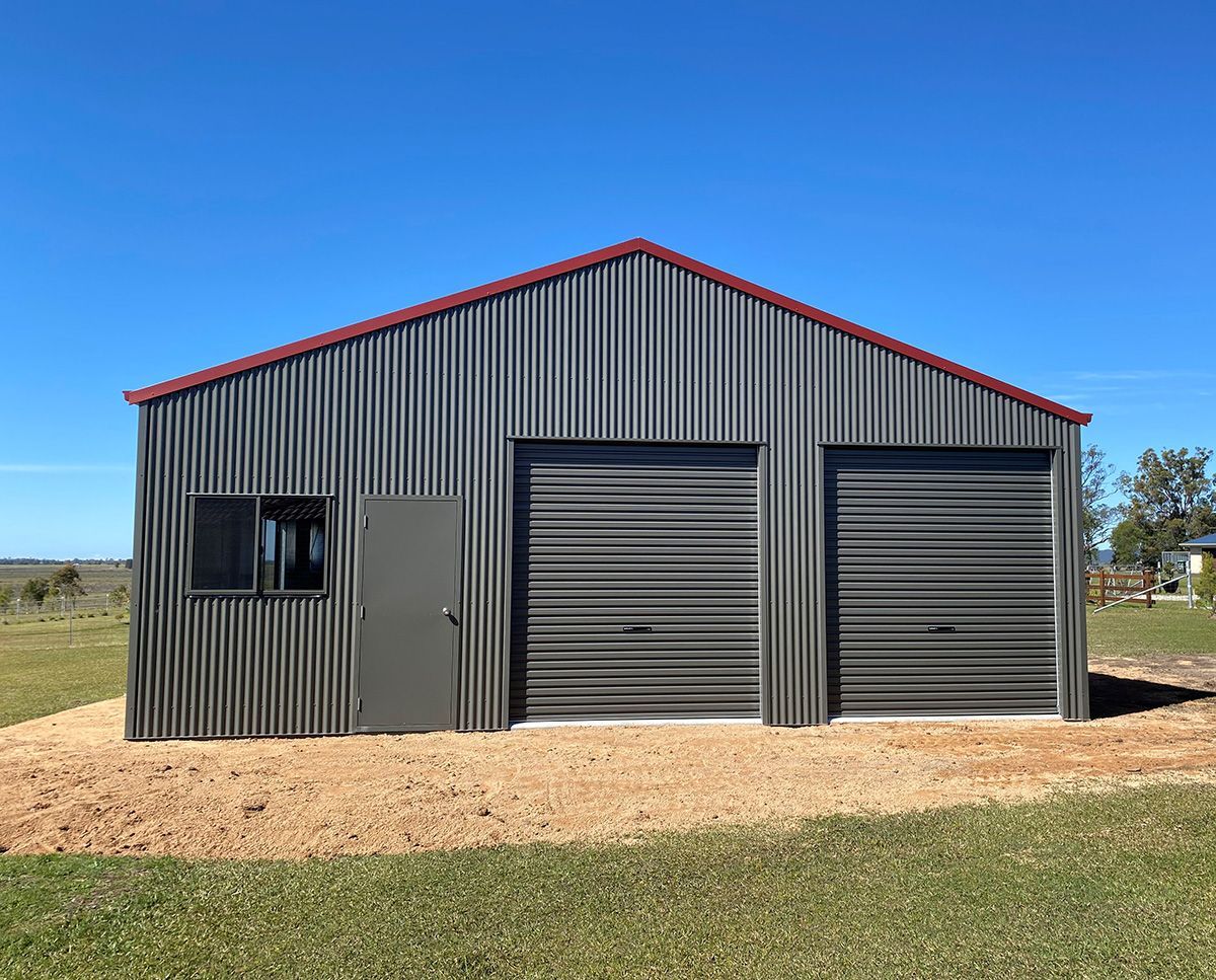 Corrugated metal shed with two garage doors and a side door, on a gravel base under a blue sky.