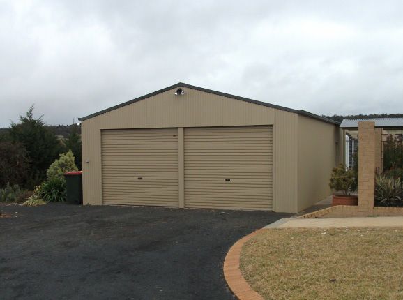 Tan Two-Car Garage With Roll-up Doors and Grass Under Overcast Sky — Northern River Sheds in Lismore, NSW