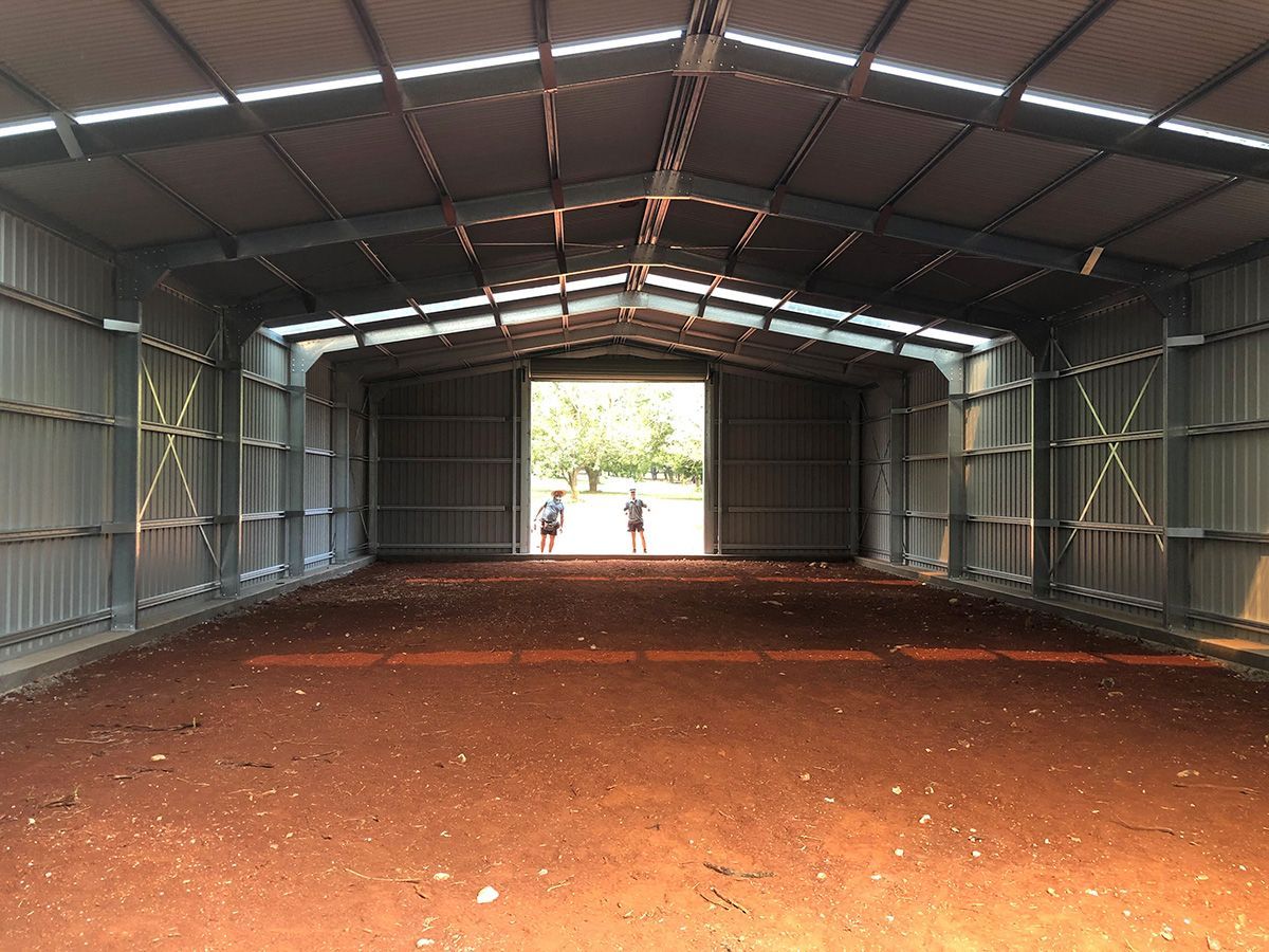 Inside of a large metal shed with open doors, two figures stand outside in the doorway.