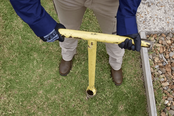 Person Using a Yellow Post Hole Digger in a Grassy Area — All Pest QLD In Sippy Downs, QLD