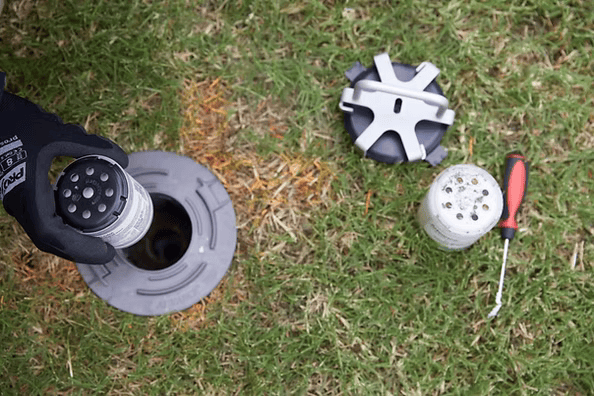 Gloved Hand Placing a Component Into a Gray In-Ground Irrigation System — All Pest QLD In Sippy Downs, QLD