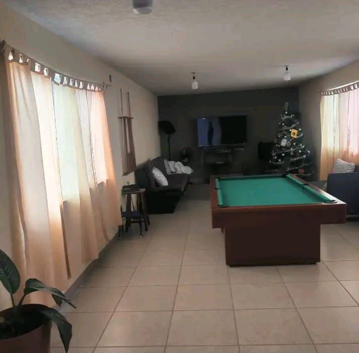 Una sala de estar con azulejos de color claro, una mesa de billar en el centro, un sofá y un árbol de Navidad en la esquina.