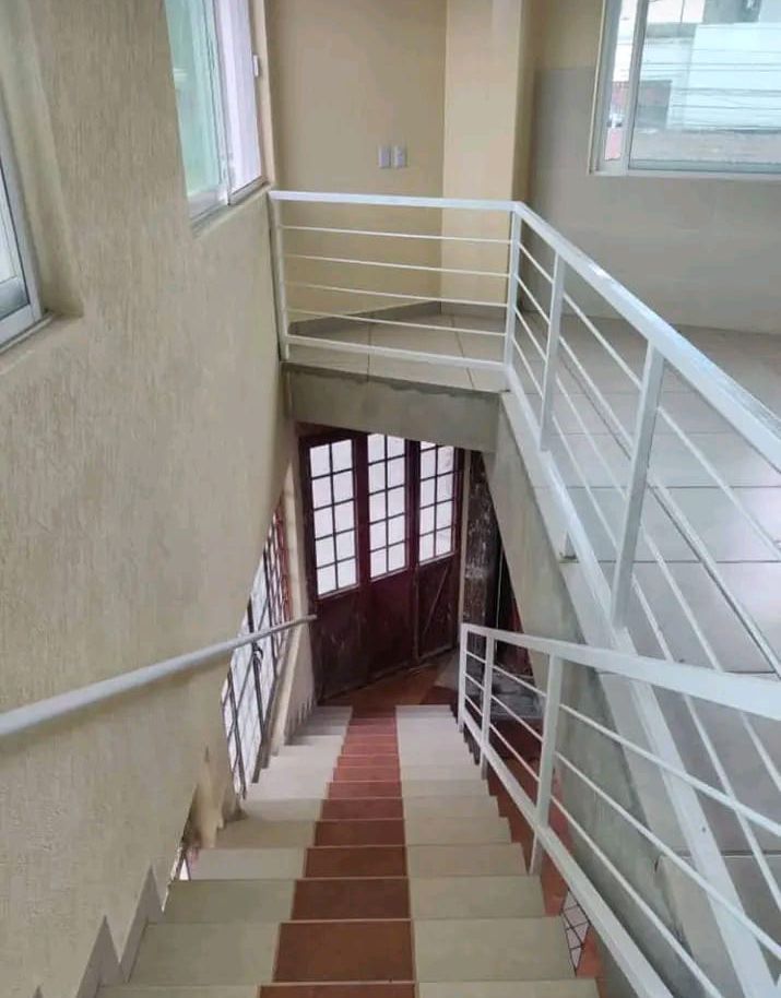 Una escalera interior con azulejos rojos y blancos conduce a unas puertas de cristal enmarcadas por barandillas blancas.