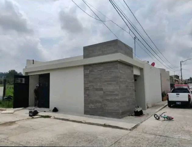 Una casa moderna de una sola planta con paredes de color beige y fachada revestida de baldosas de piedra gris, un camión estacionado y una puerta abierta en una calle.