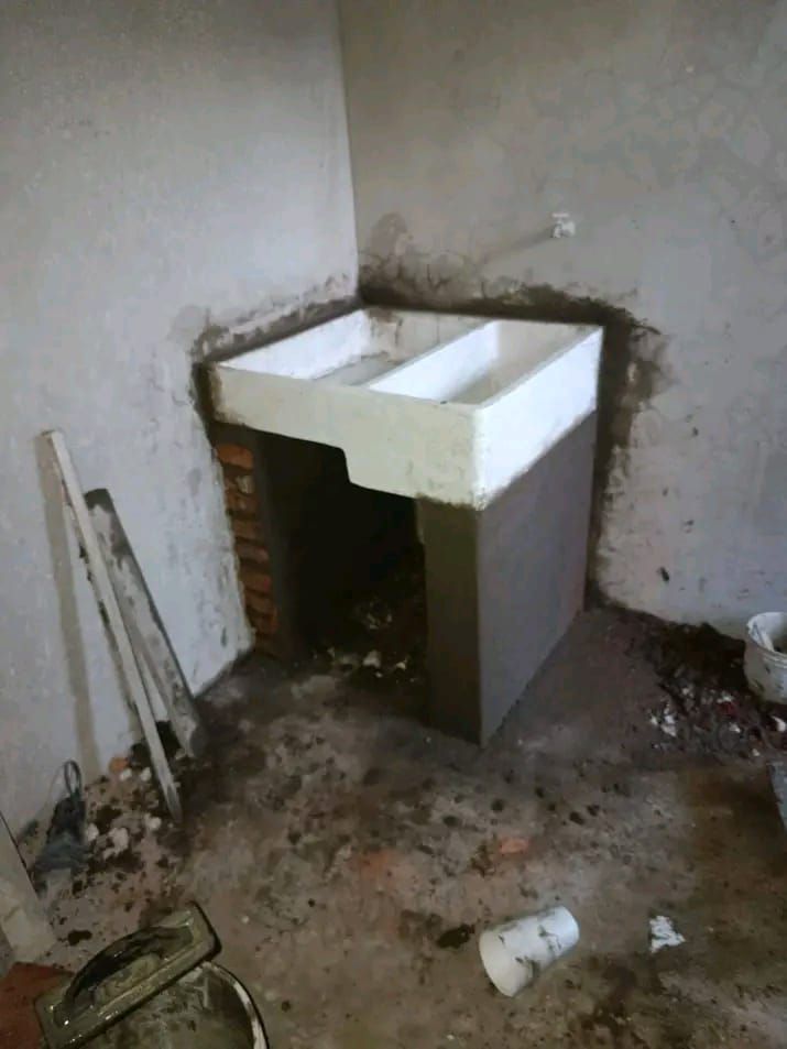 Un lavadero de hormigón de doble cubeta en construcción, ubicado en un rincón de una habitación con paredes y suelo sin terminar.