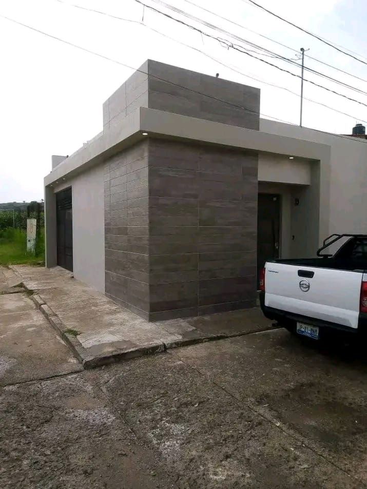 Casa moderna de una sola planta con fachada de piedra gris texturizada y una camioneta blanca estacionada en el camino de grava.