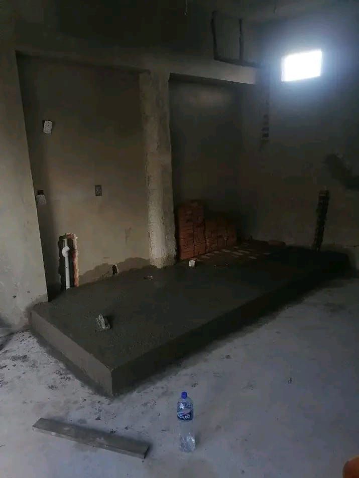 Una plataforma rectangular de hormigón en construcción en una habitación sin terminar con paredes grises y una única ventana luminosa.