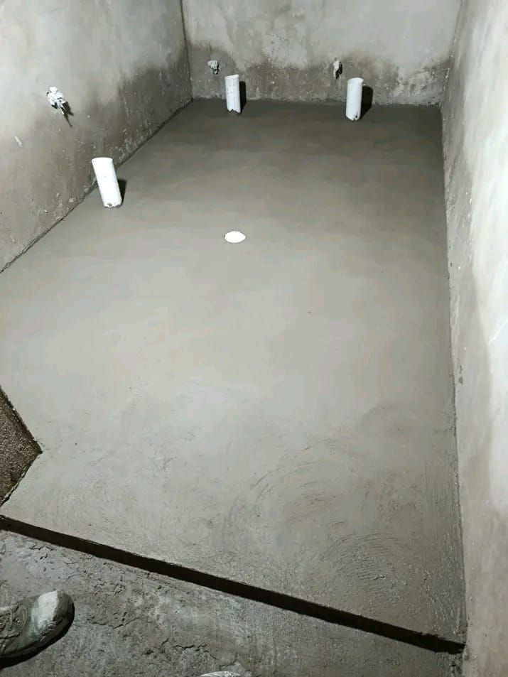 Suelo de hormigón recién vertido en una habitación sin terminar, con tuberías de fontanería que sobresalen del suelo y las paredes.