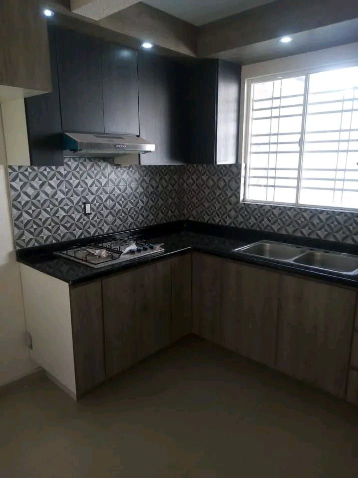 Una moderna cocina en forma de L con armarios inferiores con acabado de madera, armarios superiores oscuros, un salpicadero estampado y un fregadero.