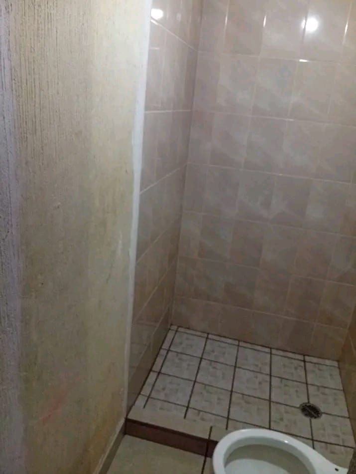 Un rincón de cabina de ducha alicatado con desagüe en el suelo y una vista parcial de un inodoro en primer plano.