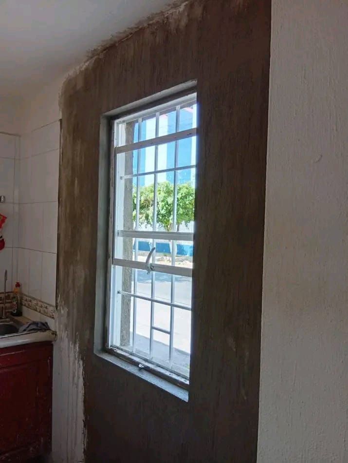 Una ventana en una pared parcialmente enlucida de una cocina. El área alrededor de la ventana tiene un acabado de yeso visto de color marrón oscuro.