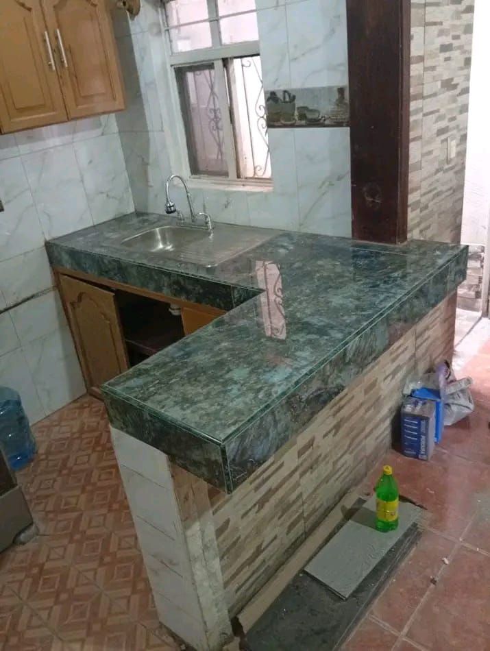 Una encimera de cocina con superficie de mármol verde oscuro y un fregadero empotrado junto a una barra de desayuno alicatada.