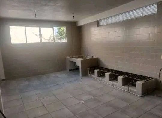 Una cocina vacía y sin terminar, con suelo de baldosas gris claro, paredes de bloques, una encimera de hormigón y una larga estufa industrial.