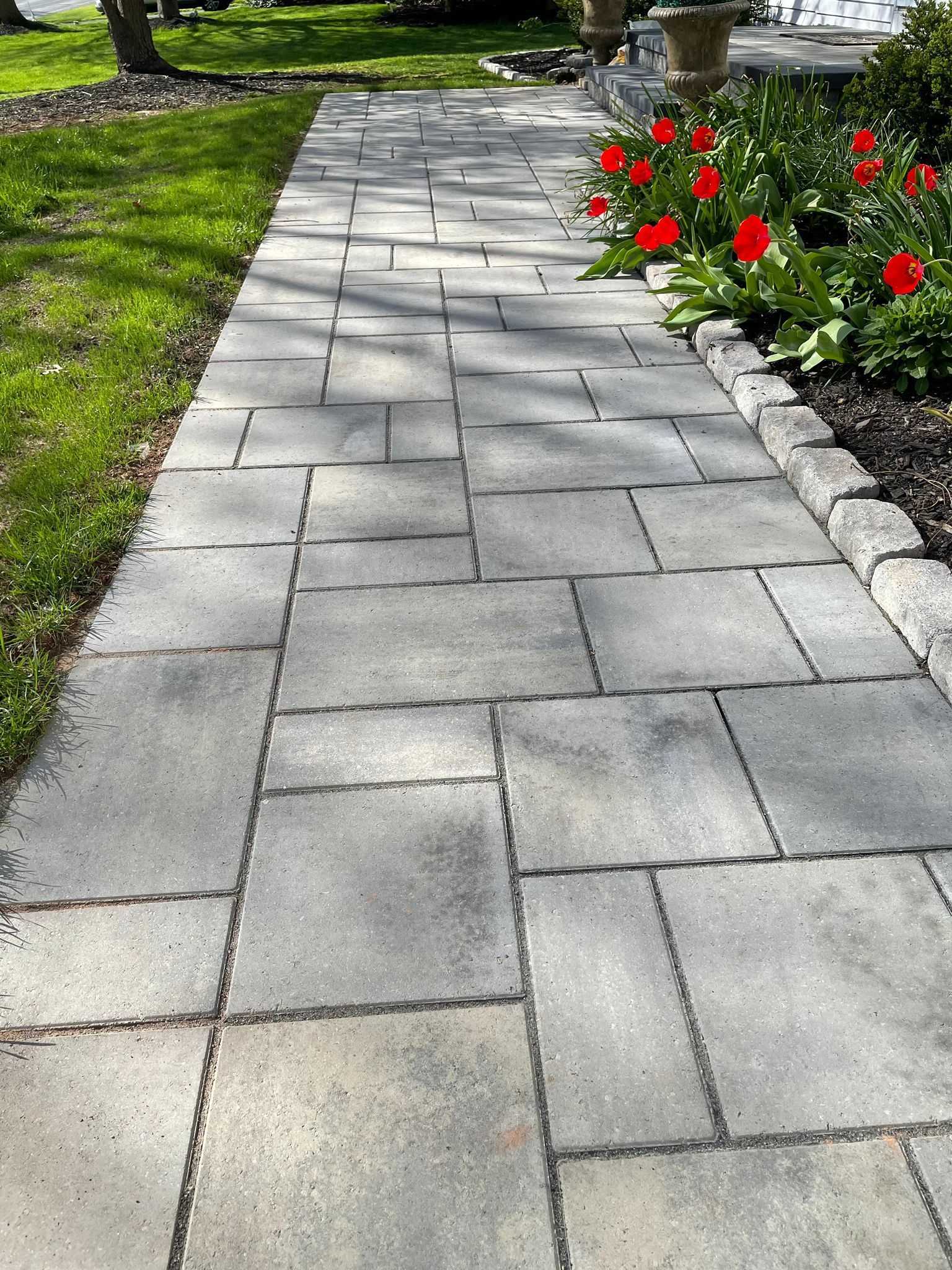 A brick walkway leading to a garden with red flowers.