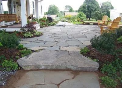A stone walkway leading to a porch with chairs.