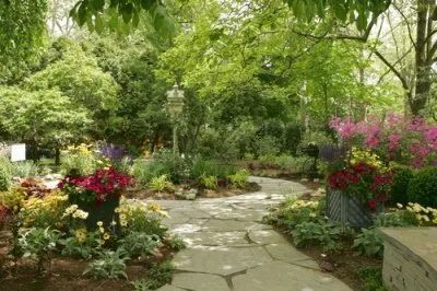 A stone path in a garden surrounded by trees and flowers.
