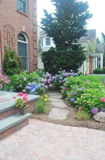 A brick walkway leading to a house surrounded by flowers