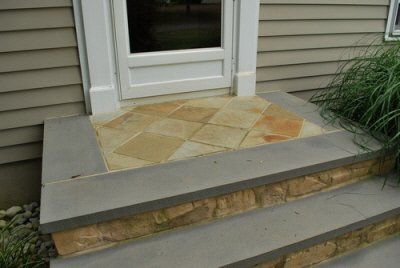A stone porch with steps leading to the front door of a house.