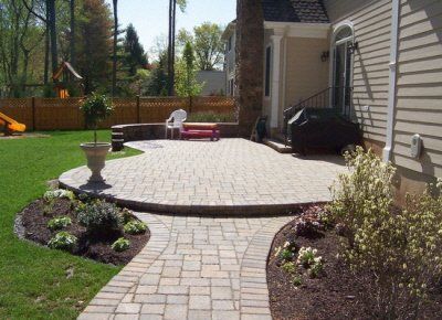A brick walkway leading to a patio in front of a house