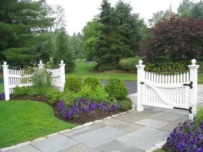 A white picket fence is surrounded by purple flowers and bushes.